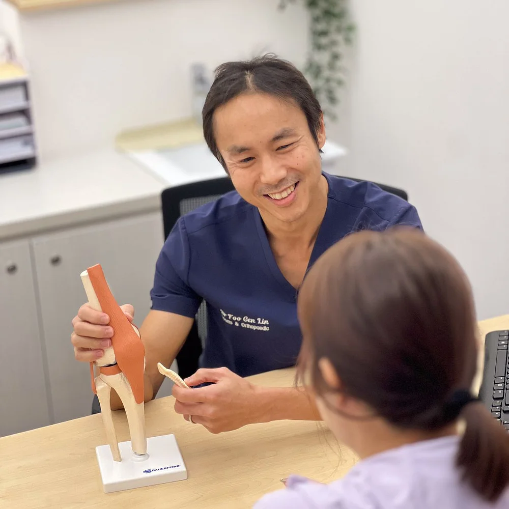 Sports doctor using a knee model to explain treatment to a patient at Apex Sports Clinic